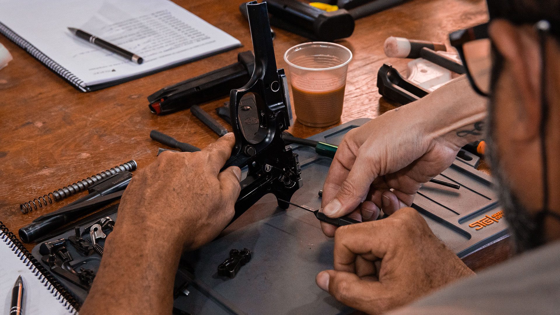 Aluno do curso de armeiro desmontando uma pistola na bancada
