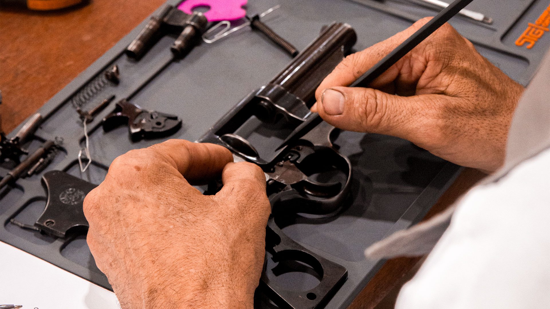 Revólver desmontado no tapete de bancada do curso de armeiro, com as peças organizadas