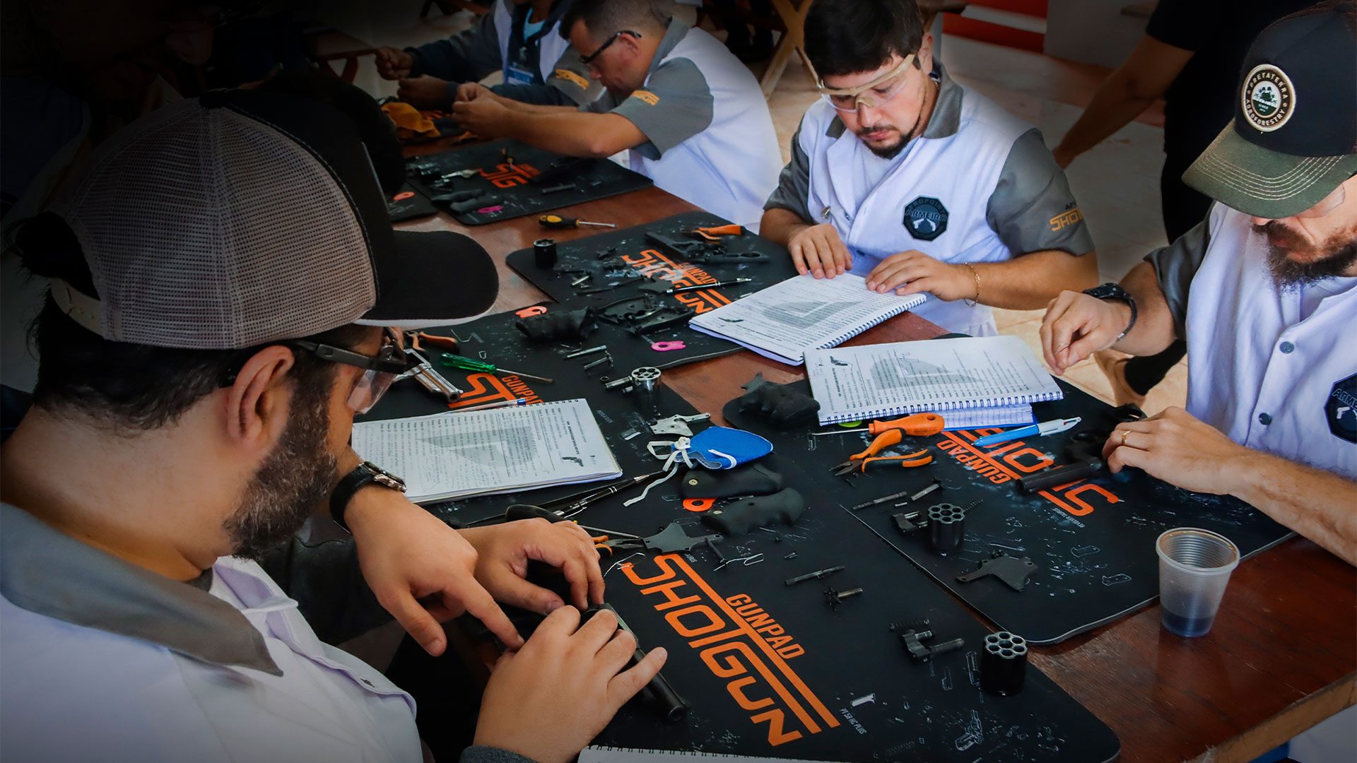 Alunos treinando desmontagem e montagem de armamento na bancada, preparação para a verificação prática de manejo
